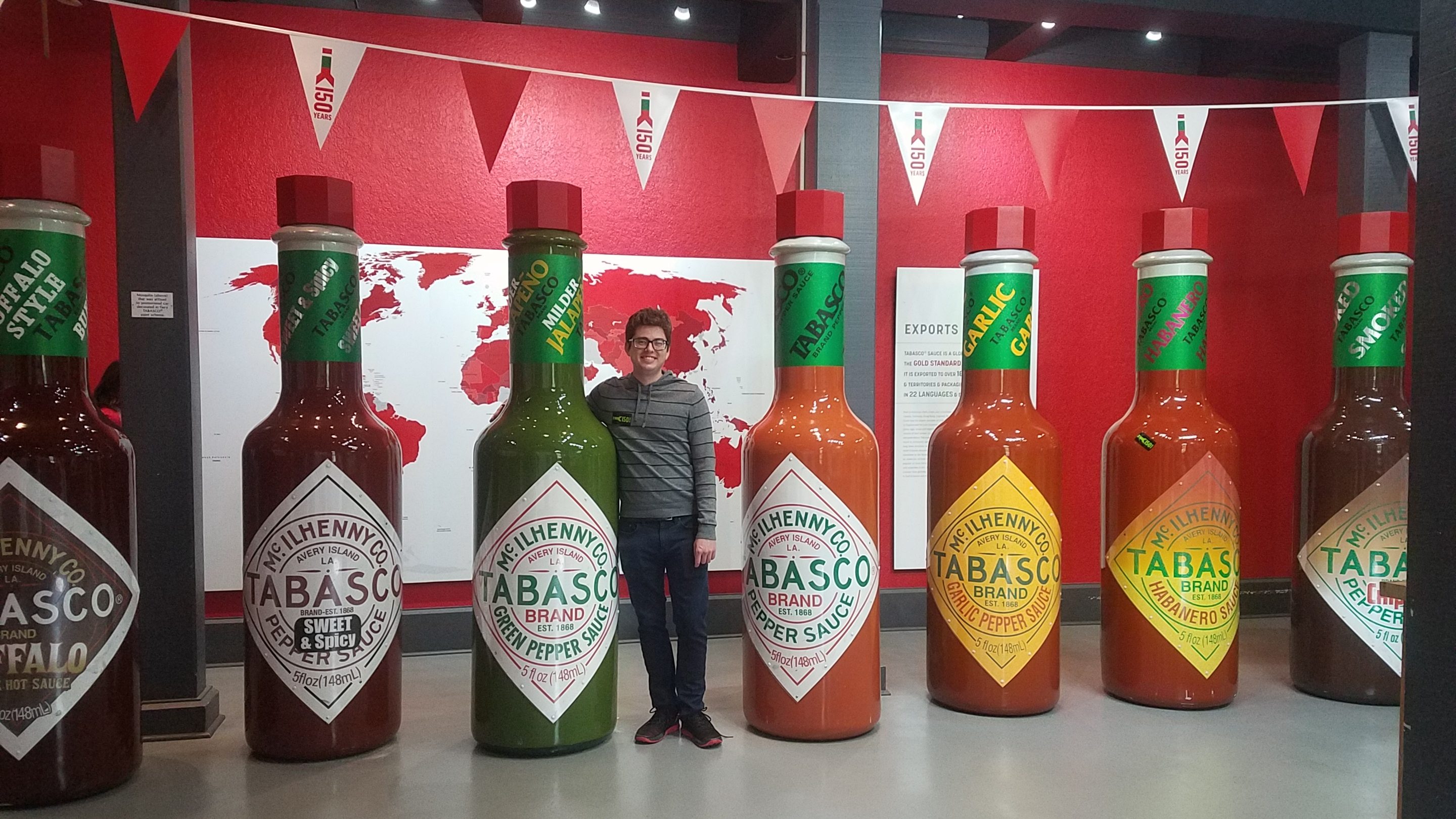Matthew posing with a row of life-size tabasco bottles, a display exhibit of tabasco's different flavors at their factory on Avery Island, LA.