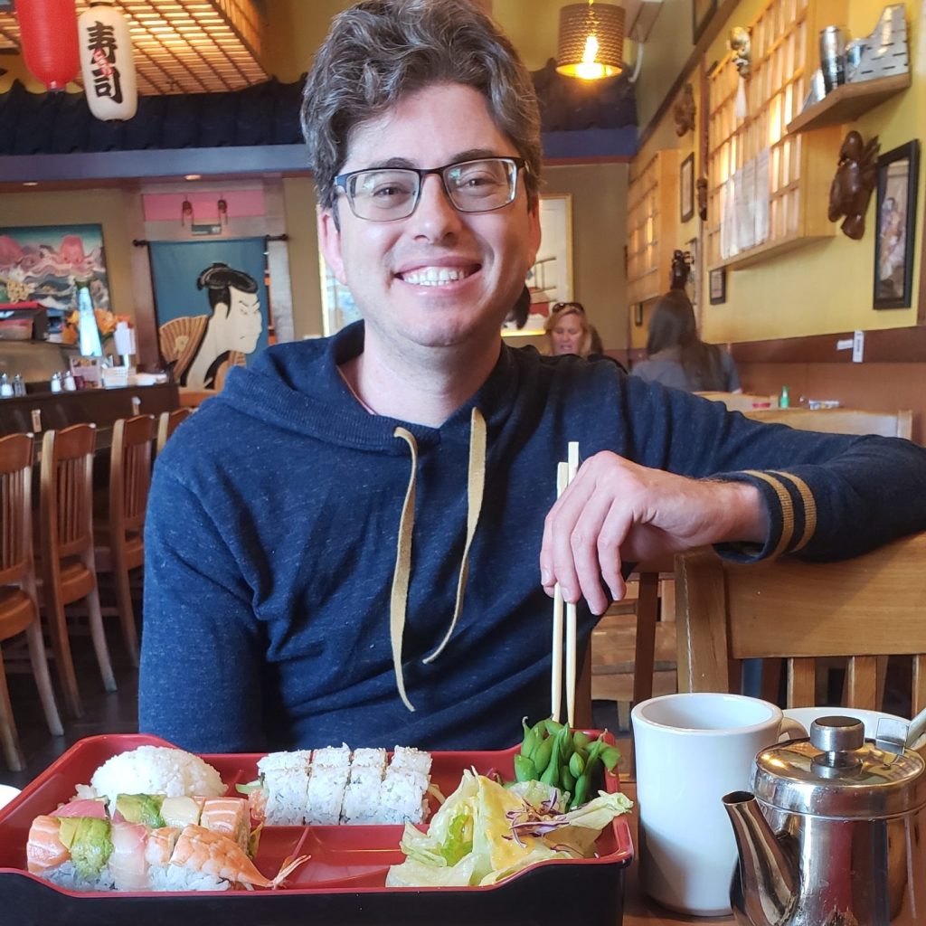 Matthew smiling, about to eat a sushi plate at Go Go Japan, a local place in our neighborhood of Oceanside.