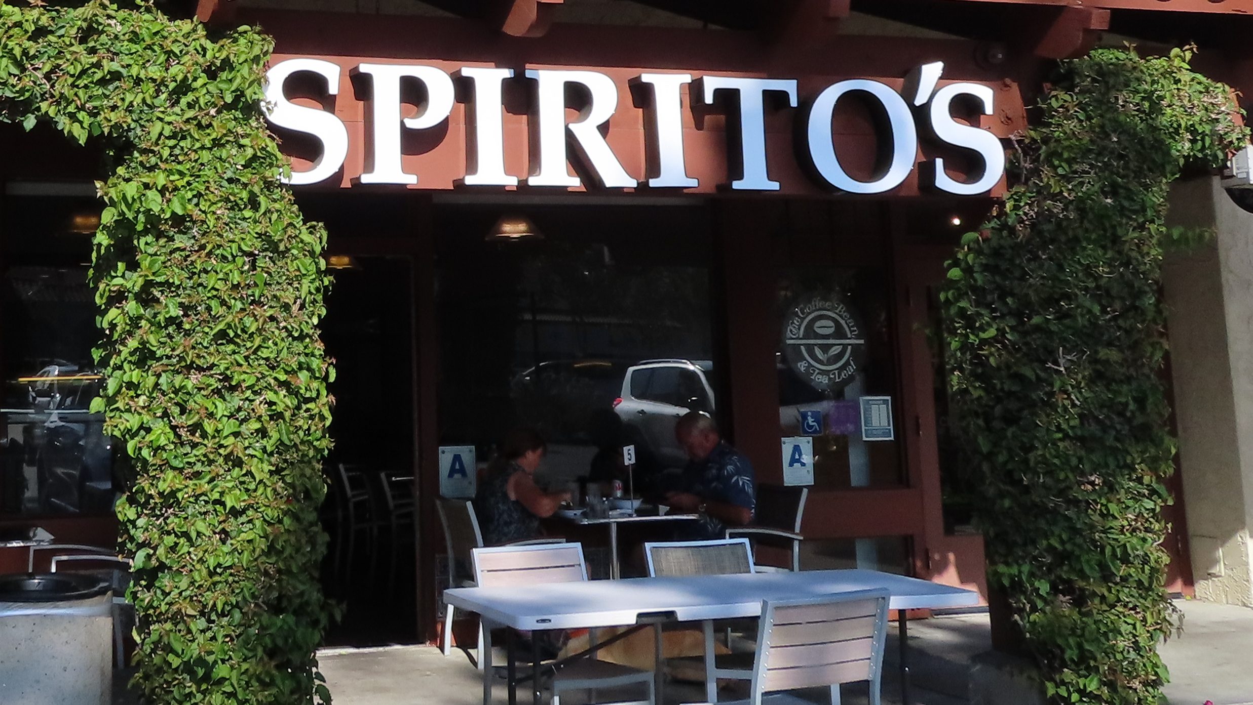 There is a sign outside the restaurant that reads in white capital letters Spirito's. There are tables outside the restaurant near the entrance and the facade is wooden with a red brick on top.