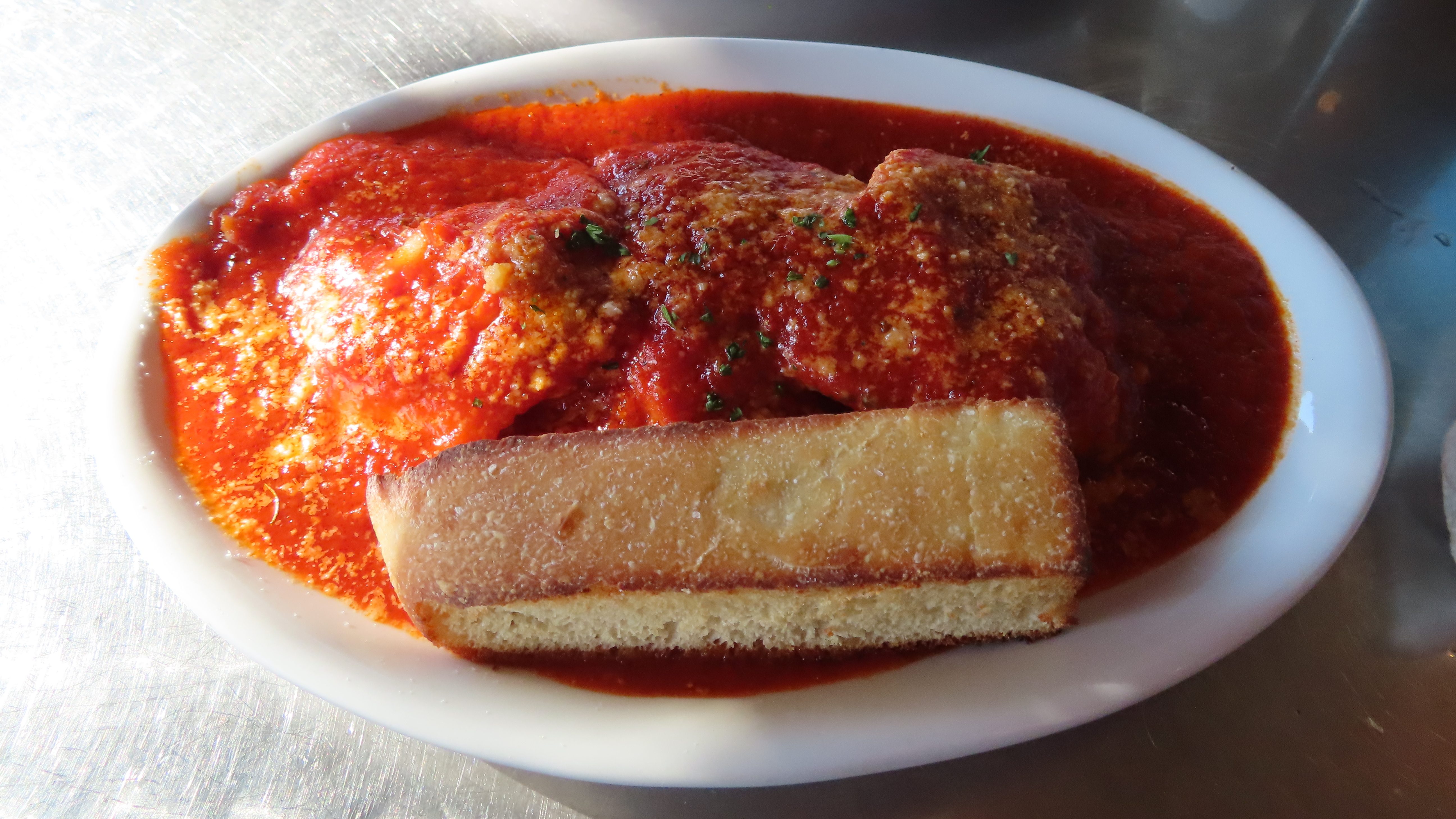 On a white plat are four large cheese ravioli smothered in a tomato gravy sauce with a piece of their toasted country bread. Their is parmesan melted on top and flakes of parsley. The ravioli looks precariously piled on one another before we dug in.