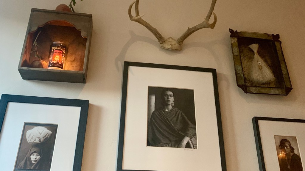 The decor on the wall above where our table was for dinner. There are seven pieces of art. The central piece is a picture of the artist Frida Kahlo. On one side of her is a portrait of a Latina women and other side a Latino man. Above her are deer antlers, to the upper left is wooden box with a votive candle and to the upper right a painting of a small figure emerging from a broom.