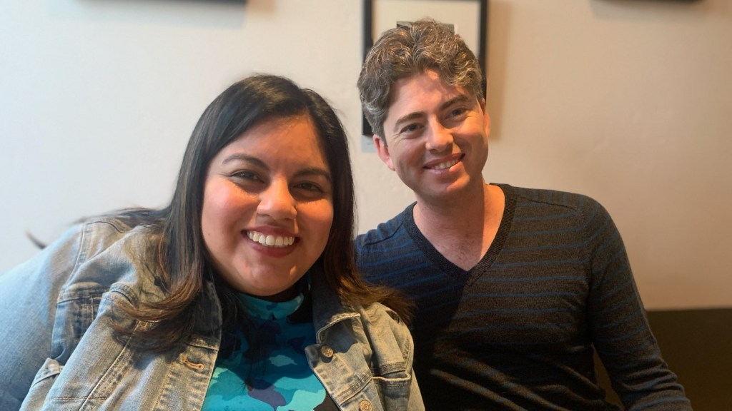 Me and Jennifer posing together at the restaurant. I'm in jeans and a v-neck light and navy blue striped center. Jennifer is to my left with a blue flower dress and jean jacket leaning into me.